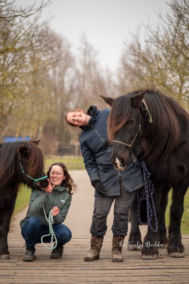 Twee vriendinnen met een donker paard en Shetland pony op een pad omringd door bomen.